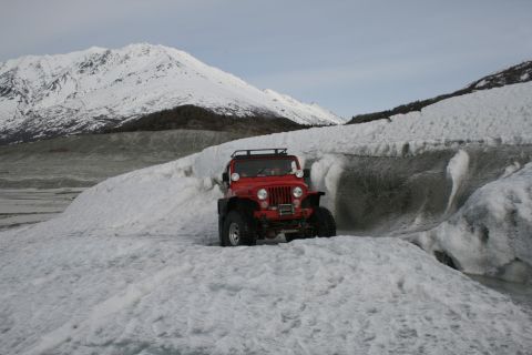 2003 Jeep TJ - A red Jeep navigates a snowy glacial landscape with snow-capped mountains in the background.