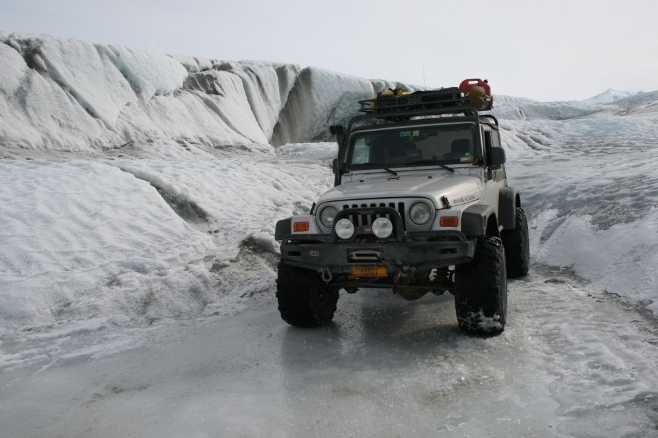 Silver 2003 Jeep Wrangler driving on a glacier with large ice formations behind it