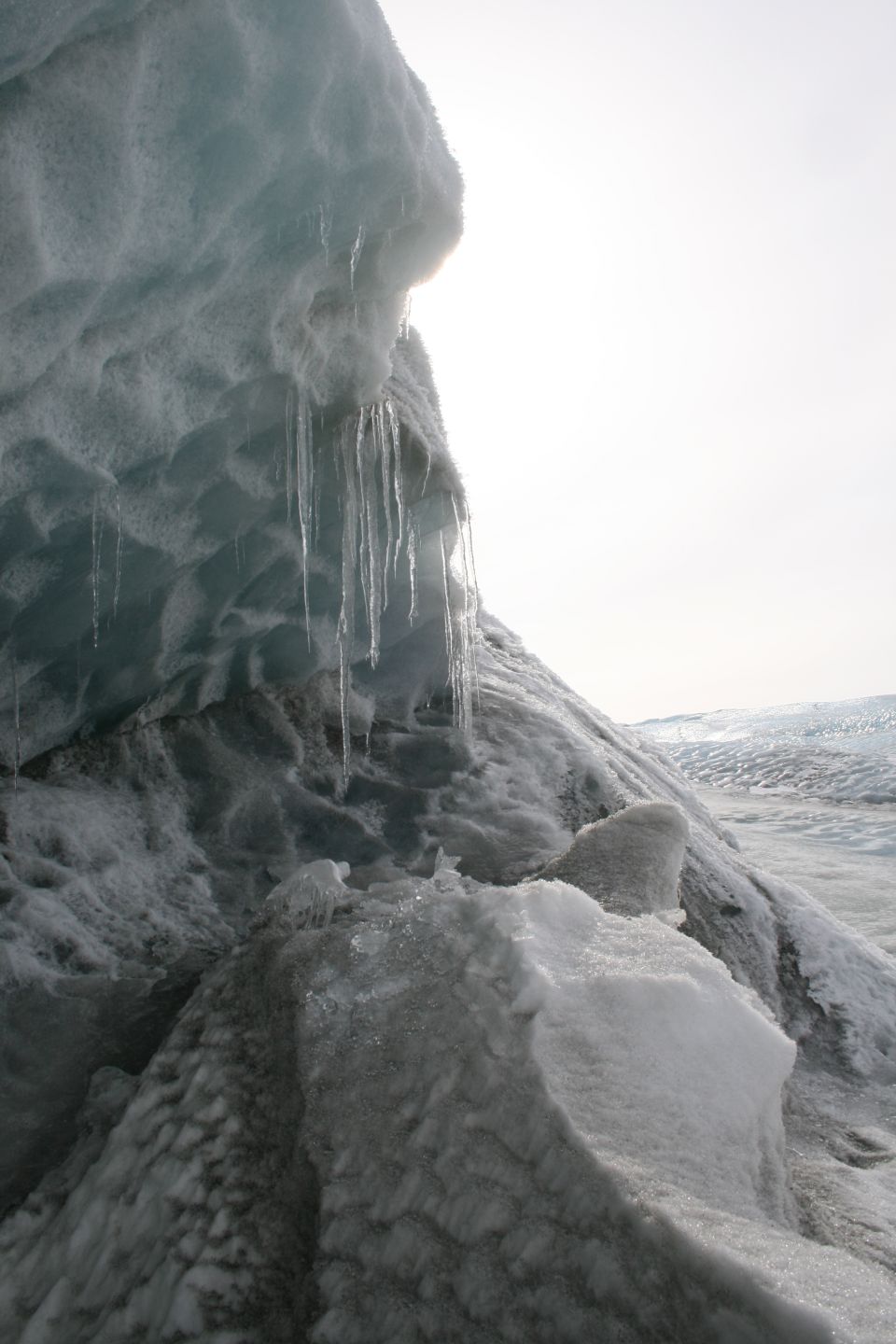 icicles hanging from a large ice formation, with more ice and snow in the background