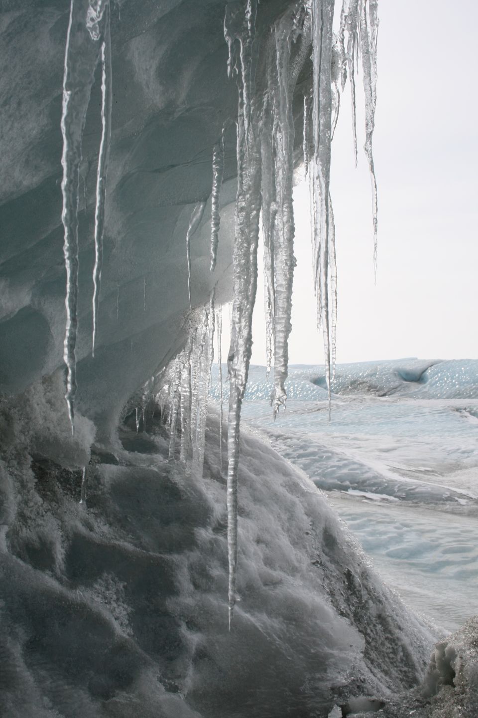 Icicles hang from a textured, icy overhang above a glacial landscape