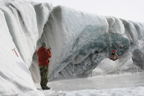 2003 Jeep TJ - A person photographs an icy glacier wall while another person sits on the ice in the foreground.