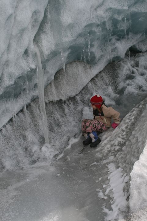 2003 Jeep TJ - A child wearing a red hat and patterned pants sits within a glacial ice cave, surrounded by ice formations and dripping icicles.