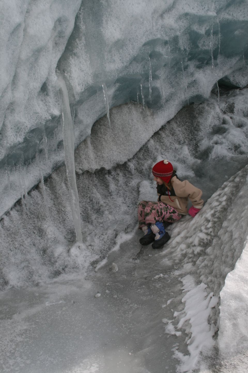Child in red hat sits in an ice cave with icicles