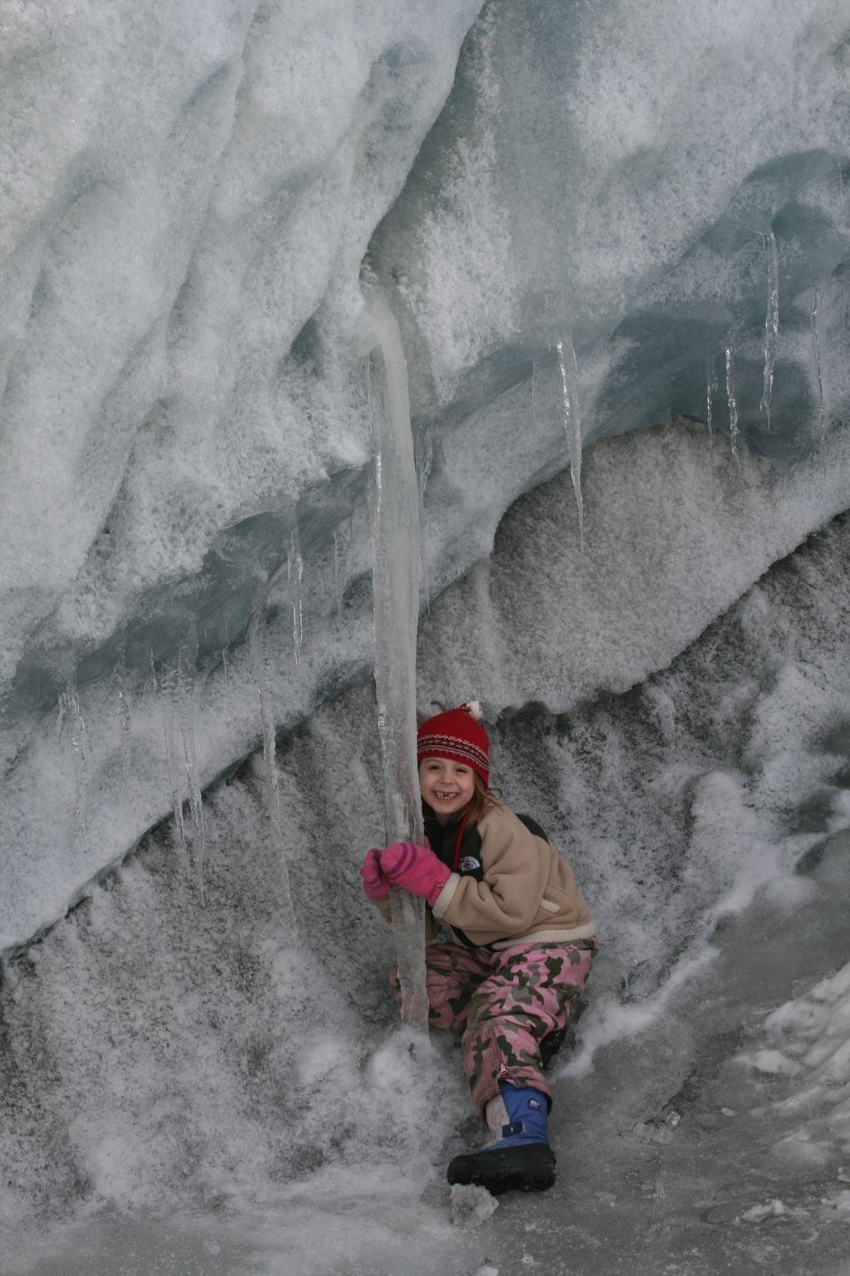 kid in red hat and pink gloves climbing in an ice cave with icicles