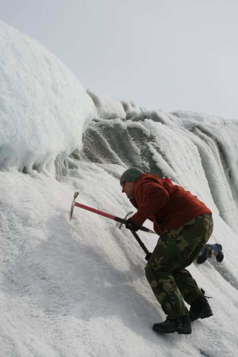 2003 Jeep TJ - A person uses ice axes to ascend a steep, icy glacier face under a cloudy sky.