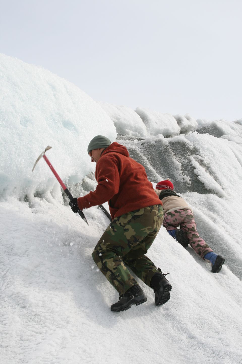 Two people with ice axes climb up a snowy, icy glacier face