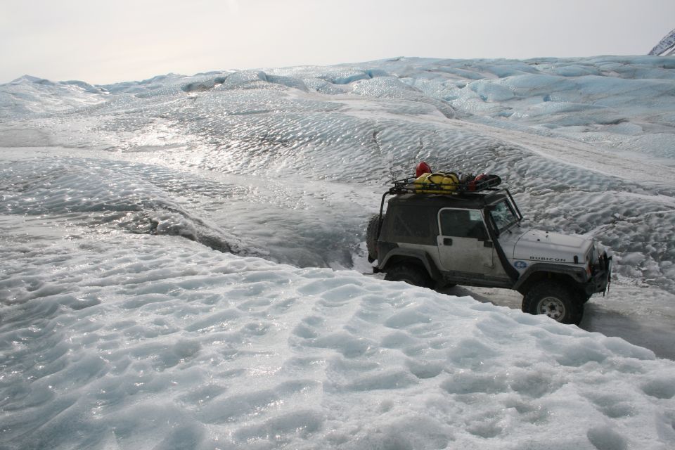 White Jeep Wrangler driving on a glacier, roof rack loaded with gear