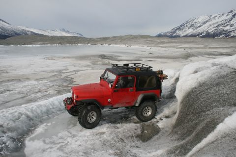 2003 Jeep TJ - A red 2003 Jeep TJ navigates an icy landscape, with snow-covered mountains visible in the distance.