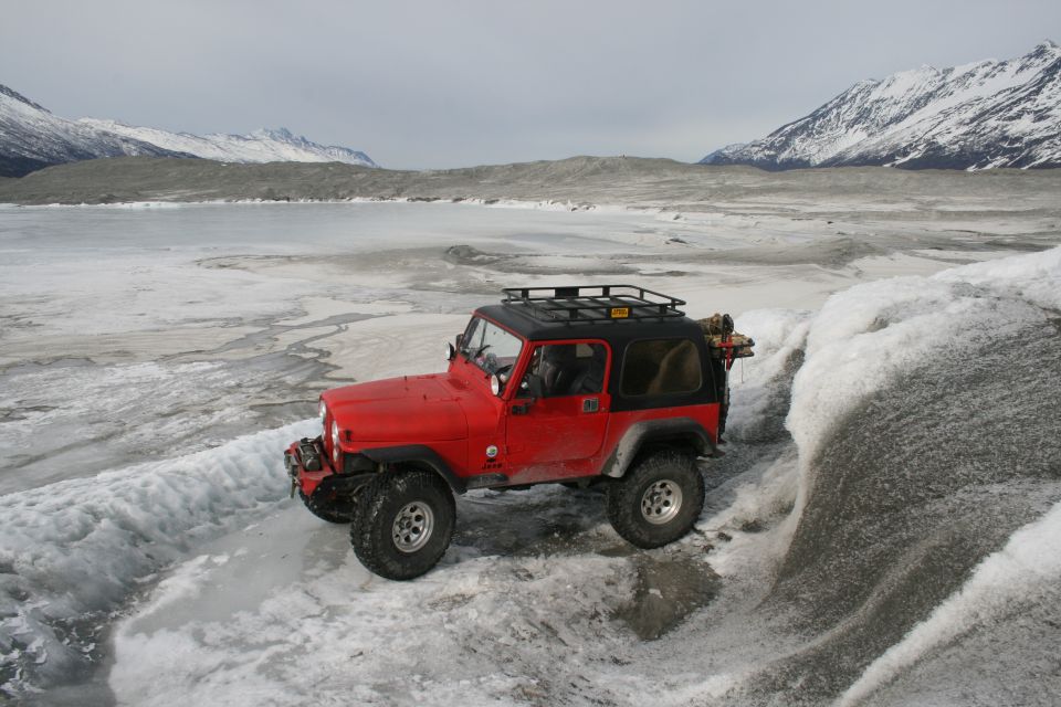 Red 2003 Jeep TJ on icy terrain with snow-capped mountains in background