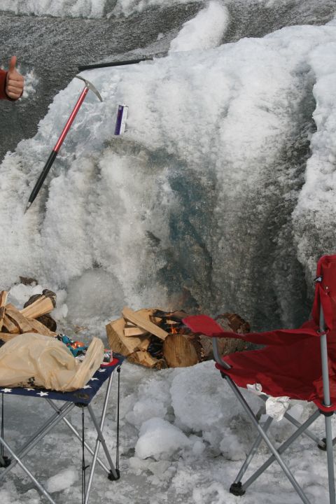 2003 Jeep TJ - Camping setup in front of a large ice formation with firewood and chairs.