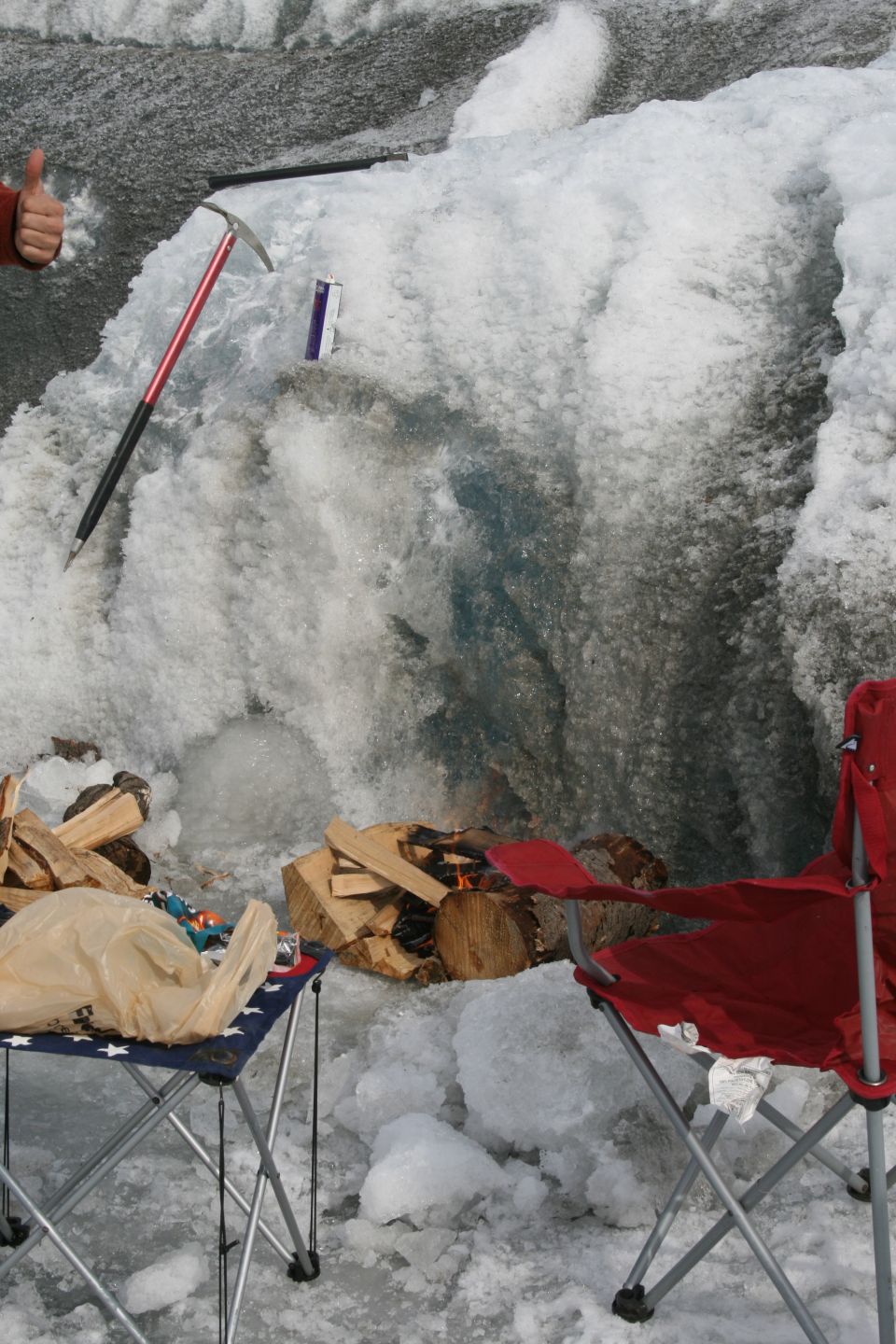 Ice wall with ice axe, purple object, firewood, and red camping chairs