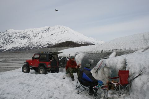 2003 Jeep TJ - A red 2003 Jeep TJ is parked on a snowy terrain near a glacier, with two people relaxing in camping chairs.