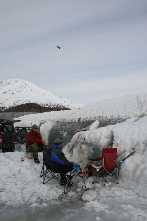 2003 Jeep TJ - People relax near a glacier, with a small plane visible in the sky above snow-covered mountains.