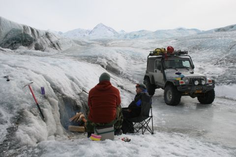 2003 Jeep TJ - Two people sit by a campfire on a glacier next to a modified Jeep Wrangler.