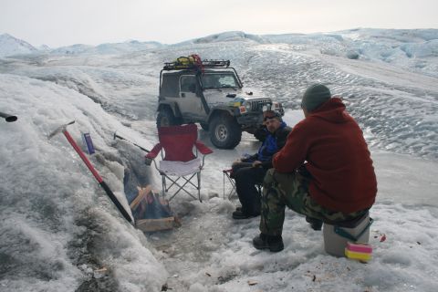 2003 Jeep TJ - A group enjoys a campfire next to a 2003 Jeep Wrangler on a vast, icy glacier.
