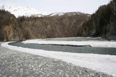 2003 Jeep TJ - A river winds through a rocky landscape with snow along its banks, framed by trees and mountains.