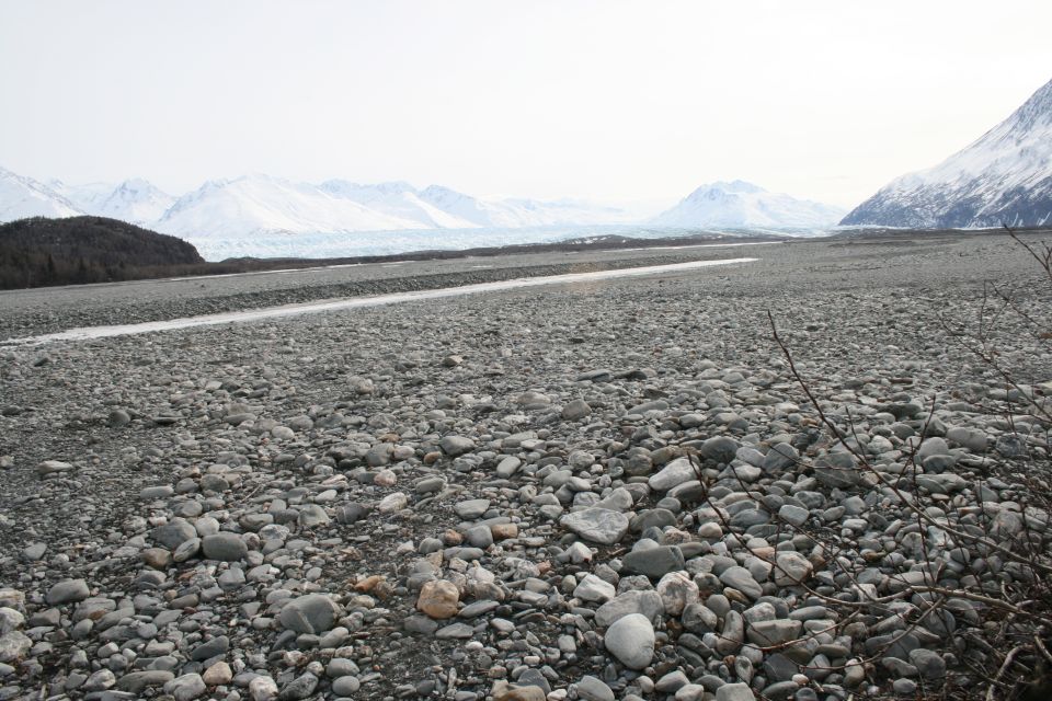 Rocky riverbed with distant snow-capped mountains and a glacier