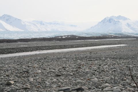 2003 Jeep TJ - A wide glacial valley with snow-capped mountains in the background under a hazy sky.