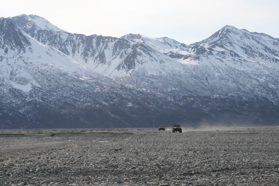 Two 2003 Jeep TJs driving on a gravelly plain with snow-capped mountains in the background