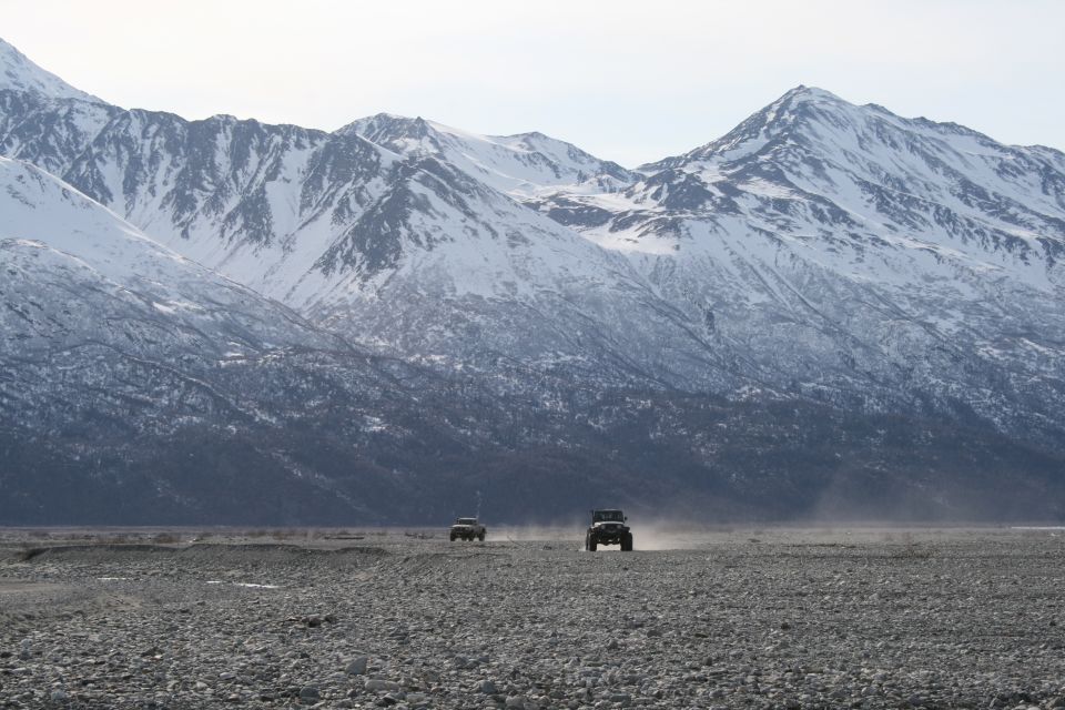 Two 2003 Jeep TJs driving on a rocky plain, front view, with snow-capped mountains behind
