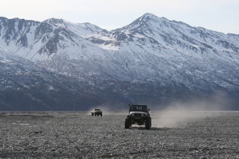 2003 Jeep TJ - Two SUVs drive across a rocky, dusty plain with a snow-capped mountain range in the background.