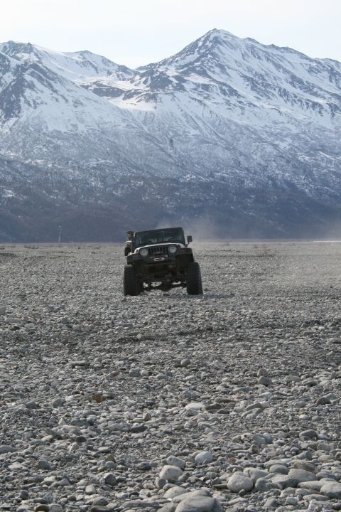 2003 Jeep TJ - A Jeep Wrangler navigates a vast, rocky terrain under a backdrop of snow-capped mountains.
