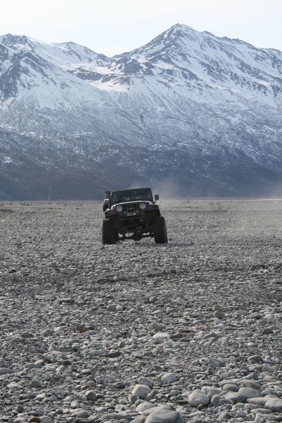 Jeep Wrangler driving on a rocky plain with snow-covered mountains in the background