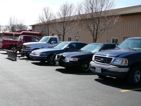 1997 Mercury Grand Marquis - Several vehicles are parked in a lot outside a building, including a plow truck and police cars.
