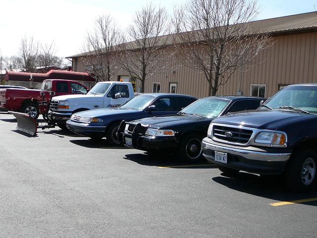 Parked vehicles including a red pickup with a plow, a white pickup, a blue sedan, a black police car, and a dark blue Ford F-150