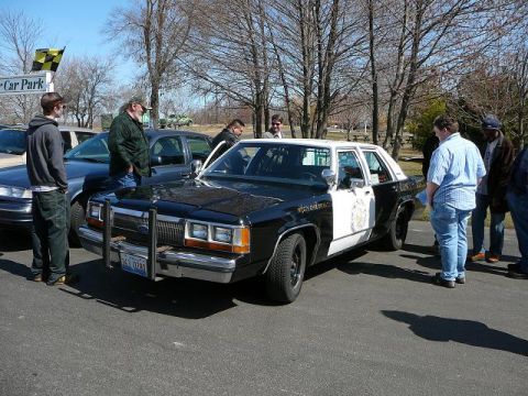 1997 Mercury Grand Marquis - A police car with a two-tone paint scheme is parked on asphalt, with people standing around it.