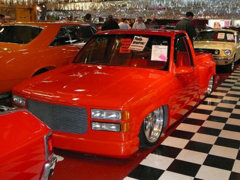 1997 Mercury Grand Marquis - A bright red pickup truck is displayed at a car show, with other vehicles visible in the background.
