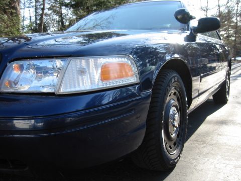 2003 Ford Crown Victoria - Close-up of a dark blue sedan's front quarter panel and headlight assembly on a sunny day.