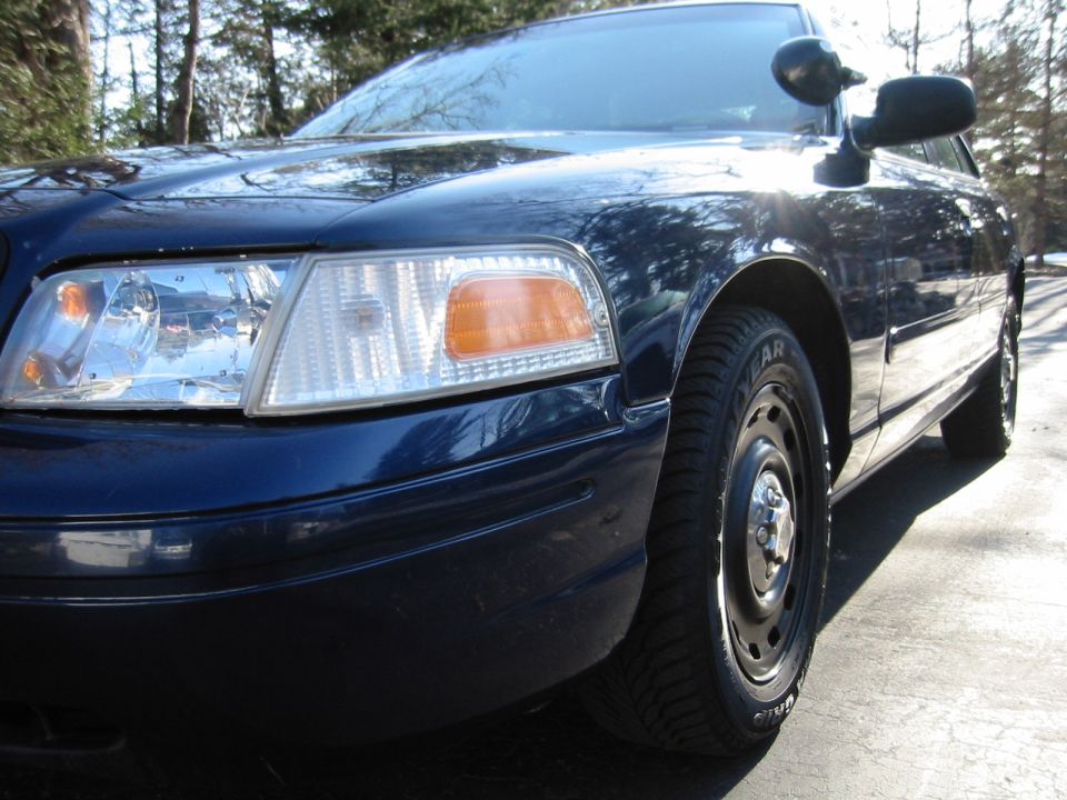 Dark blue sedan, front fender and headlight visible. Looks like a 2003 Ford Crown Victoria