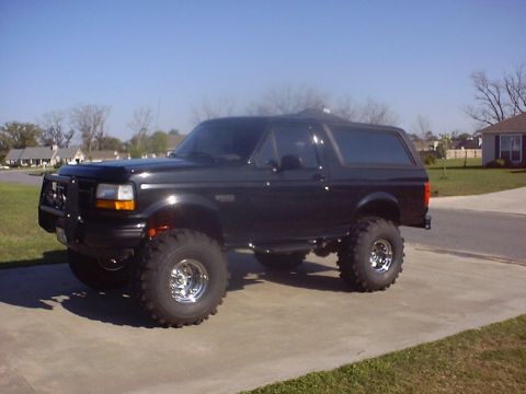 1995 Ford Bronco - This lifted black Ford Bronco is parked on a concrete driveway under a clear blue sky.