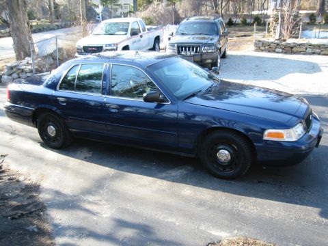 2003 Ford Crown Victoria - Blue 2003 Ford Crown Victoria parked on a paved surface, with other vehicles in the background.