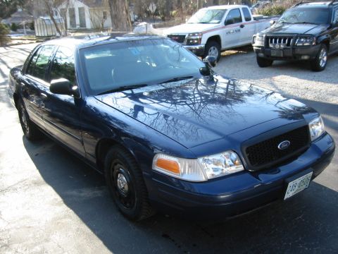 2003 Ford Crown Victoria - A dark blue Ford Crown Victoria police car is parked on a street with other vehicles behind it.