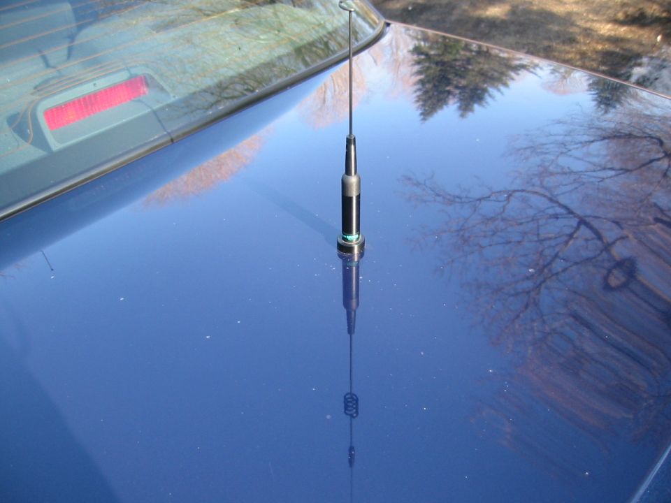 Black car antenna with green accent ring mounted on the hood of a blue car