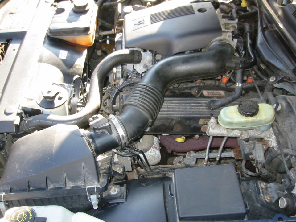 Engine bay with air intake, hoses, and engine components visible. Some rust on exhaust manifold