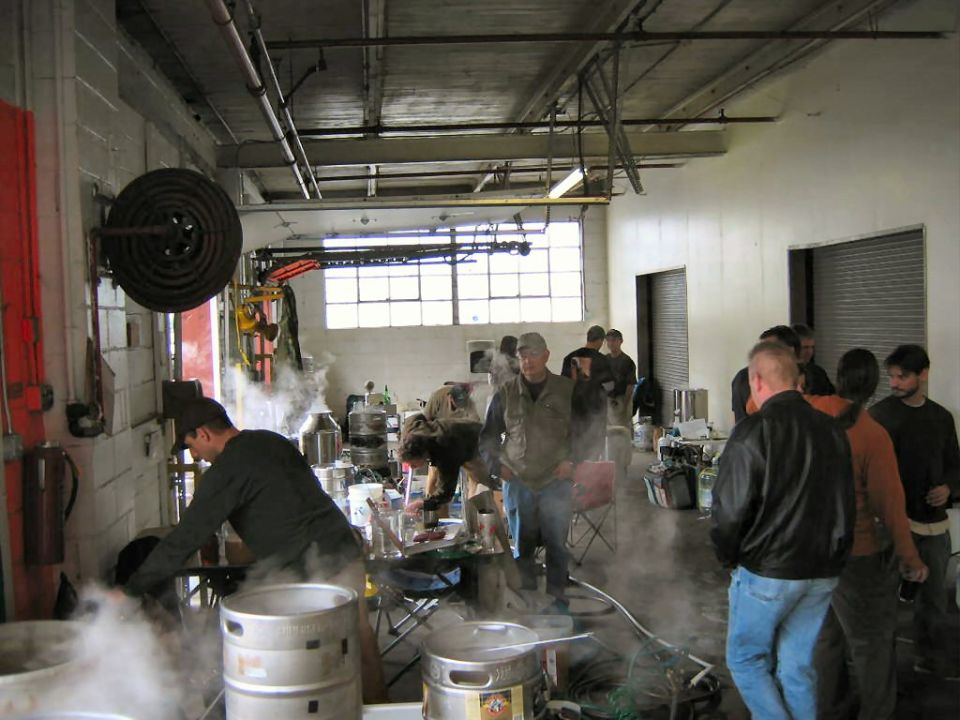 People gathered in a workshop, some tending to large metal vats and equipment emitting steam