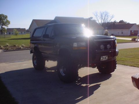 1995 Ford Bronco - Lifted 1995 Ford Bronco parked on a driveway under a bright sun.