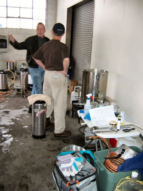 1985 Ford LTD Crown Victoria - A group of people are gathered around brewing equipment in what appears to be a workshop or garage.