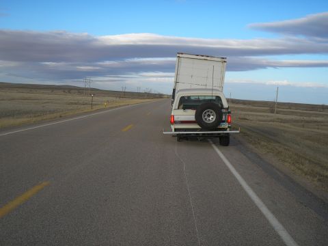 1990 Ford Bronco - Ford Bronco towing a trailer down a long, empty highway under a cloudy sky.