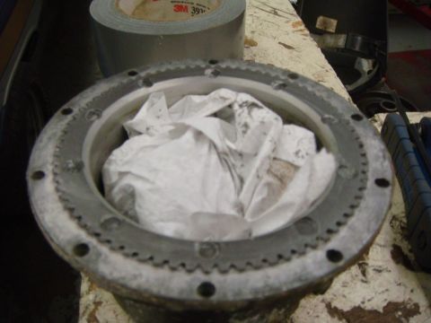 1996 Ford Bronco - A metal component, possibly a hub or differential cover, is stuffed with paper towels and sits on a workbench next to a roll of duct tape.