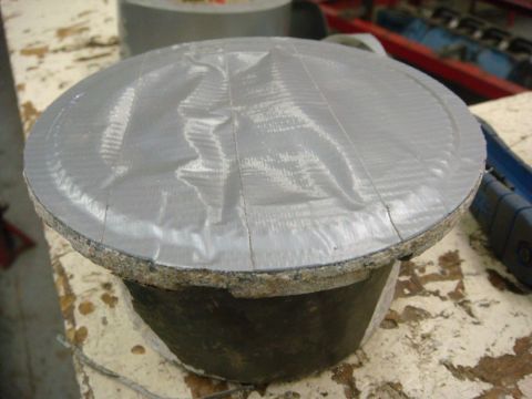 1996 Ford Bronco - A close-up view of a round object covered in gray duct tape, resting on a workbench.