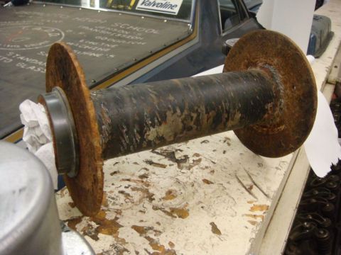 1996 Ford Bronco - A rusty metal spool with flanges sits on a workbench, with a dark vehicle visible behind it.