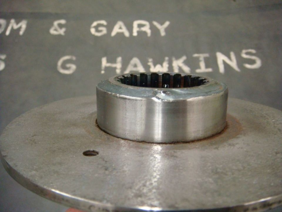 Metal part with splines, possibly a hub or adapter, with text 'TOM & GARY' and 'G HAWKINS' visible in the background