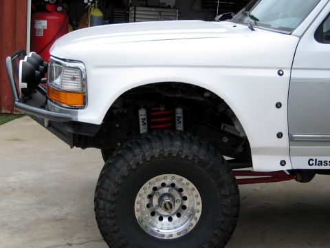 1996 Ford Bronco - Close-up front-corner view of a white 1990s Ford full-size truck/Bronco lifted on a coilover suspension, with a red coil spring flanked by…