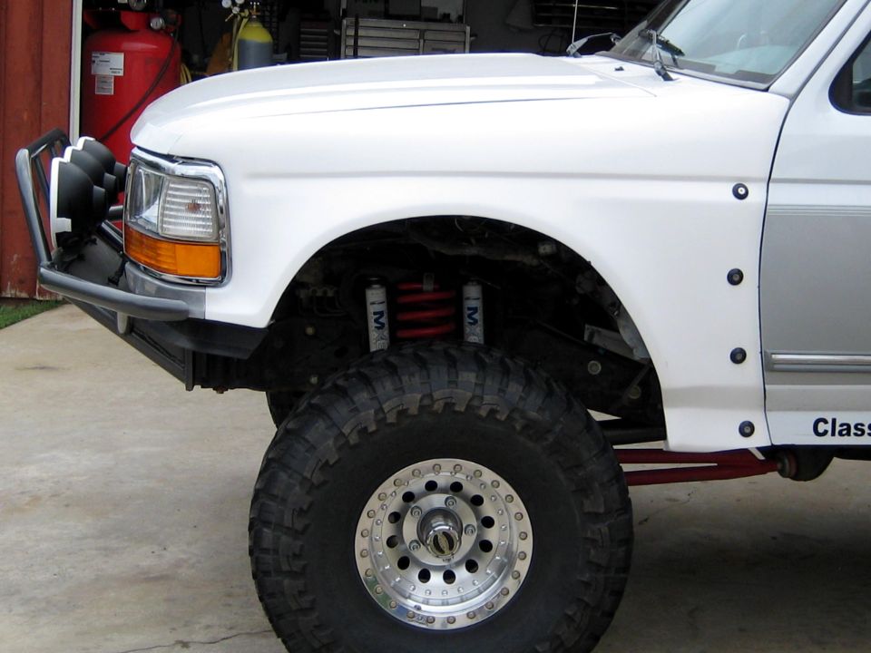 Lifted white Ford Bronco front corner showing coilover shocks, red coil and beadlock wheel