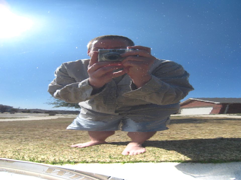 Man in shorts and shirt takes a selfie with a camera, reflected in a shiny surface