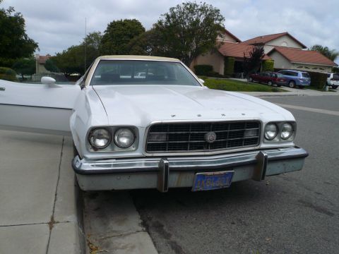1975 Ford Ranchero - A white 1975 Ford Ranchero with a tan vinyl top is parked curbside with its driver's door ajar.